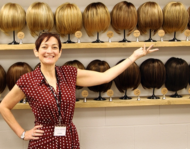 Emma from Simply Wigs standing with a wide range of wigs available for consultations and appointments.