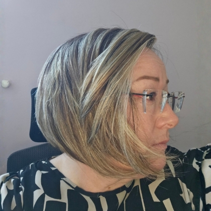 Side profile of a woman with an angled, chin-length bob in blended blonde and brown with highlights, wearing glasses