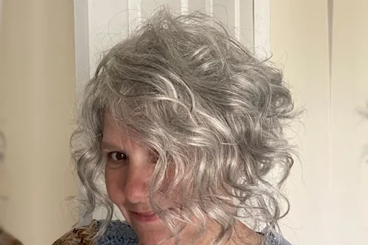 Lady wearing waved soft grey wig with a side-swept fringe.