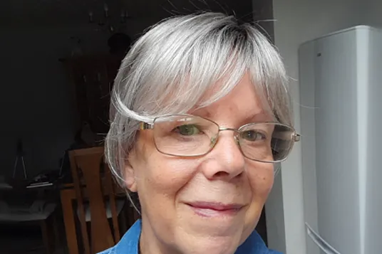 Woman with glasses wearing the Hawaii Mono Lace Deluxe wig in Rooted Grey, a short layered grey style with a side-swept fringe