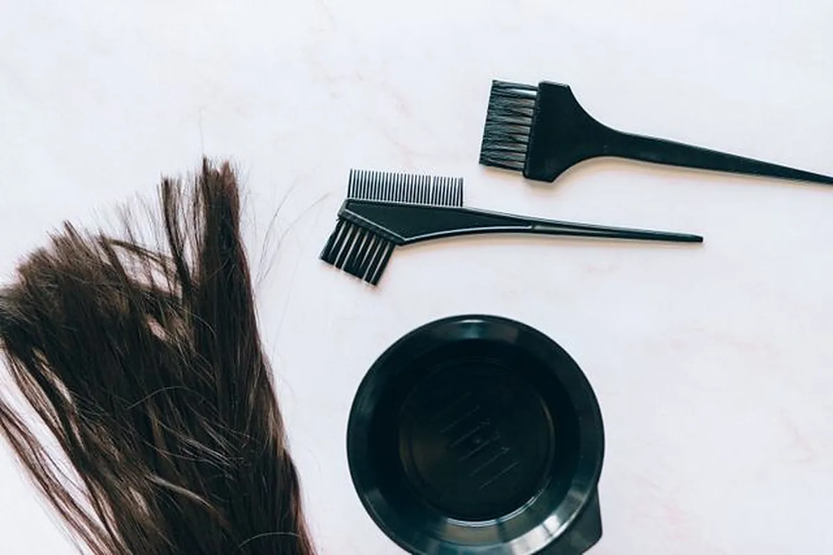 Lock of brown hair beside two tint brushes and a black colour bowl on a white surface