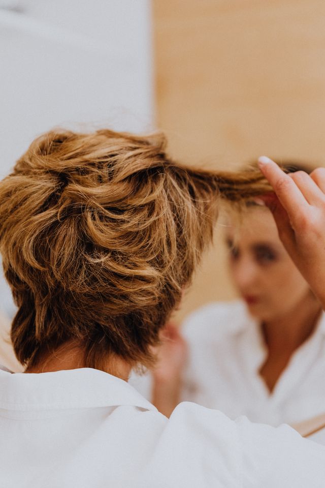 Woman looking in the mirror and pulling her hair, illustrating trichotillomania and hair loss caused by compulsive hair pulling.